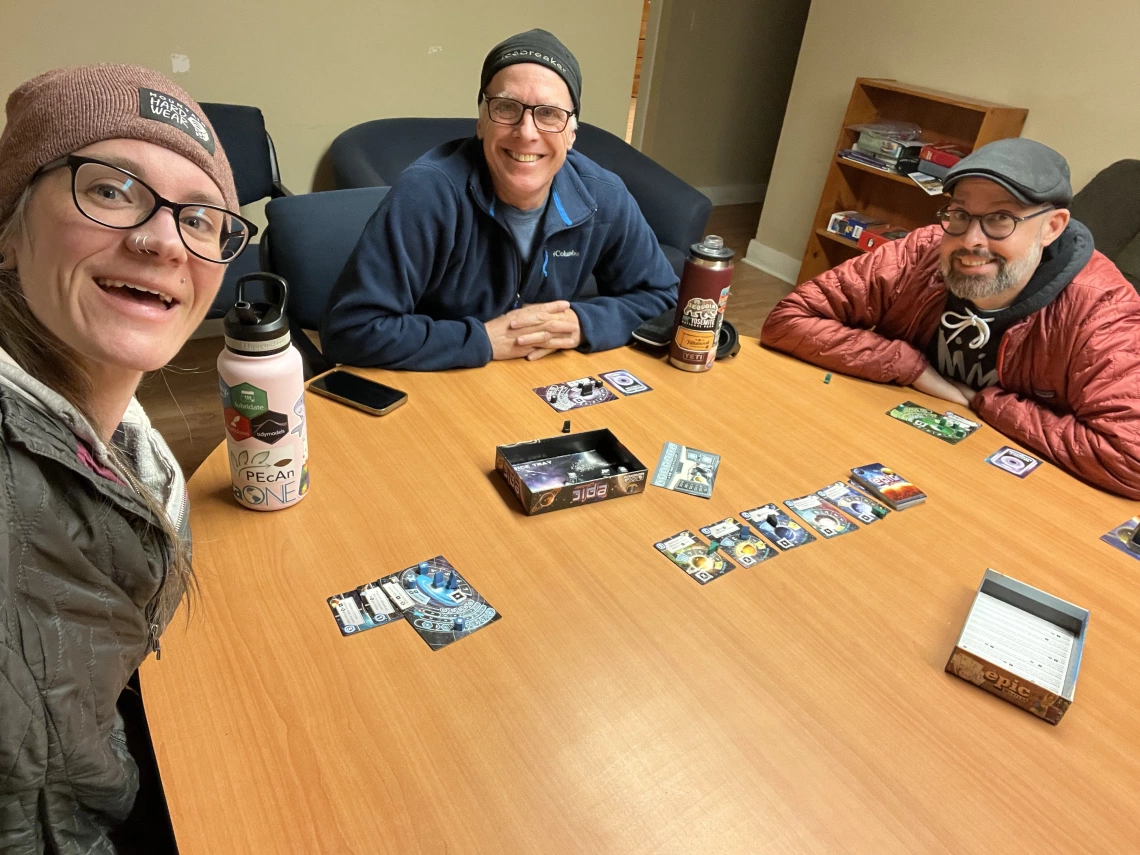 3 people sitting around a table playing a board game